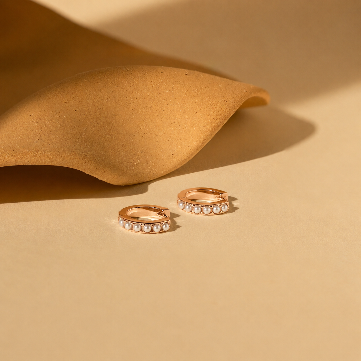 Two rose gold hoop earrings with small diamonds on a beige background
