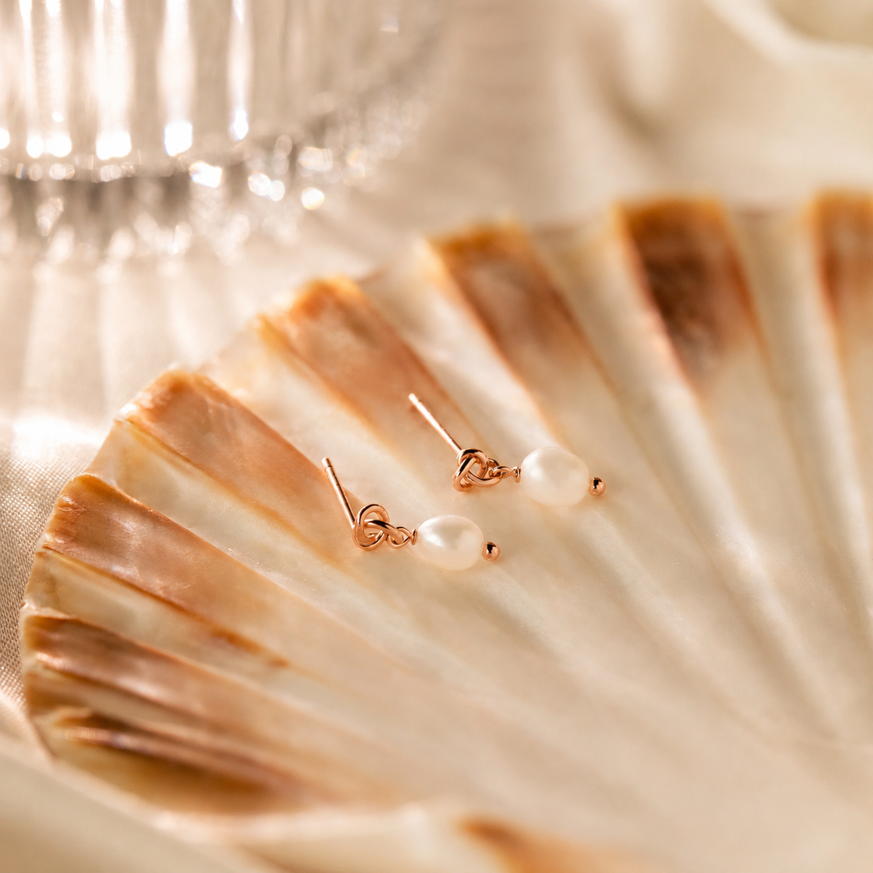 Pair of pearl earrings with rose gold accents on a shell