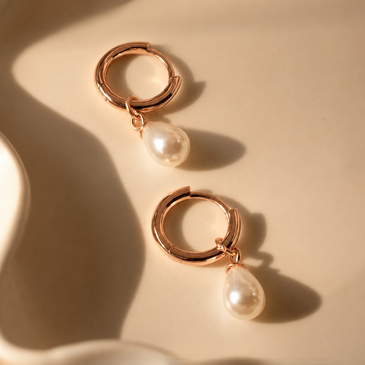 Gold hoop earrings with pearl drops on a beige background