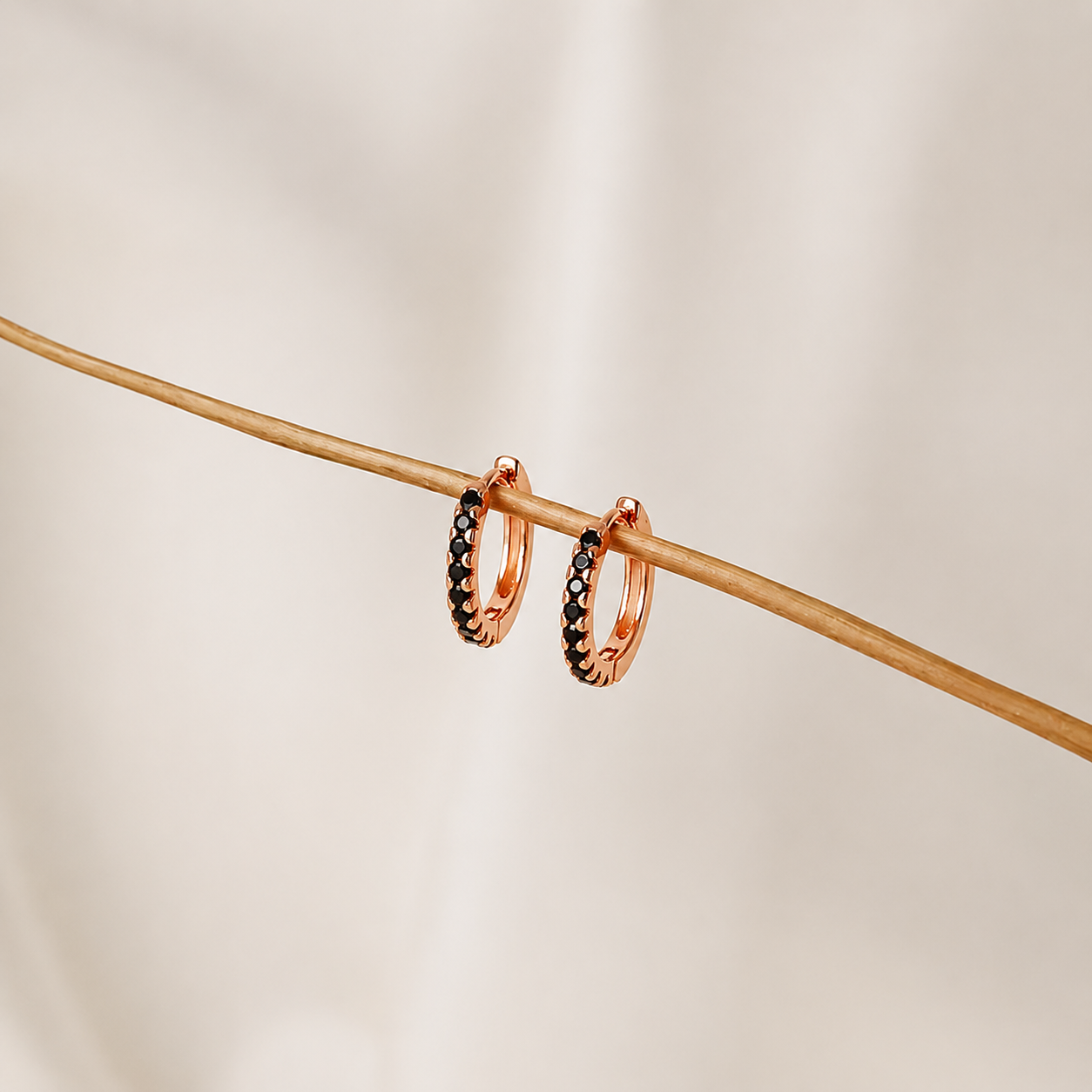 Rose gold hoop earrings with black gemstones on a beige background