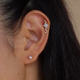 A person wearing star-themed ear cuffs on both ears, with the outer cuff of the right ear being gold-colored and adorned with multiple stars, while the inner cuff is silver and simple. The left ear features a silver cuff with a similar star design.