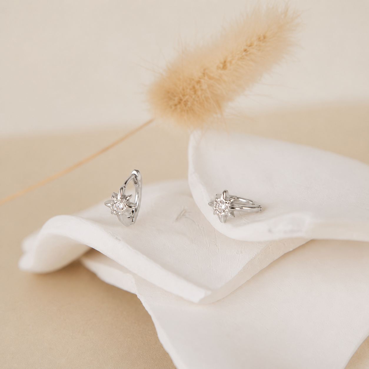 Silver earrings on a white fabric with a soft beige background