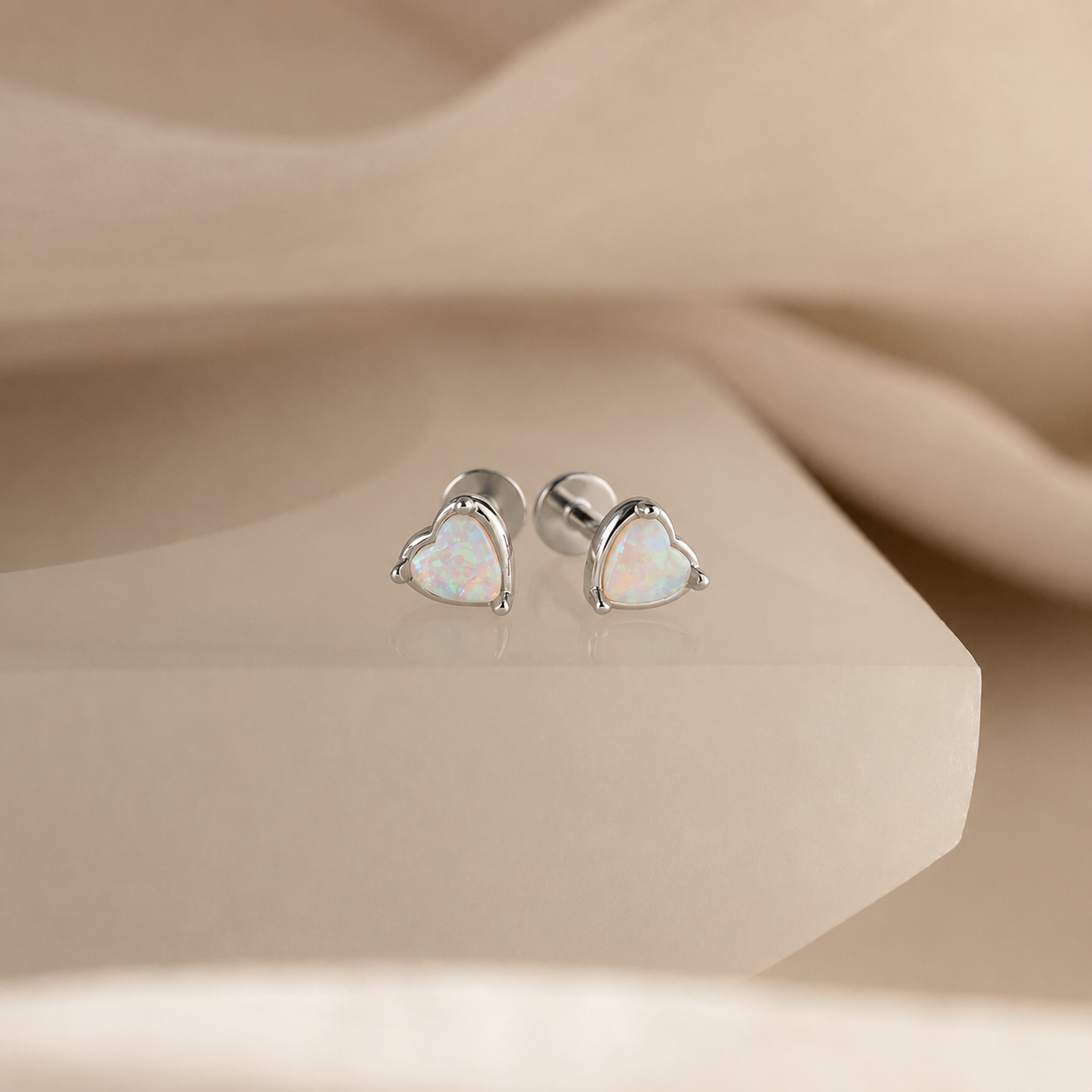 Heart-shaped opal stud earrings on a beige surface