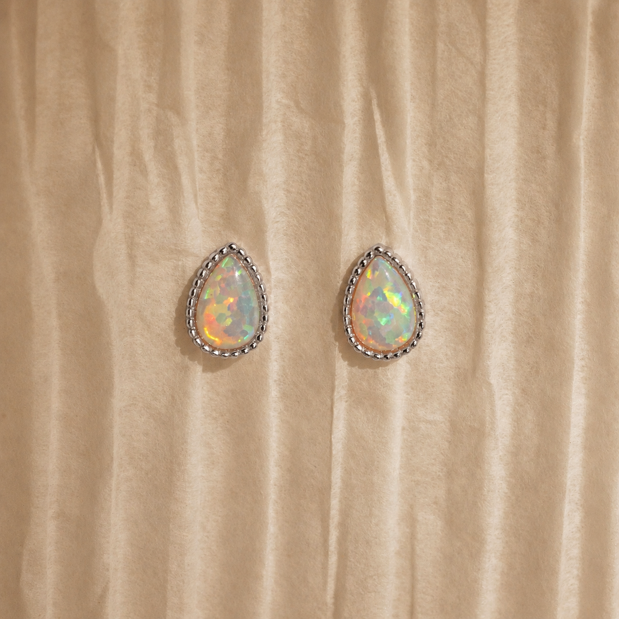 Teardrop-shaped opal earrings on a beige fabric background
