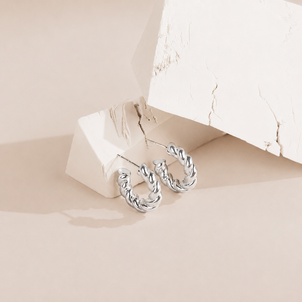 Silver hoop earrings on a beige surface with a soft focus background
