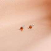 Pair of orange gemstone stud earrings on a beige fabric background