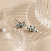 Pair of silver earrings with blue gemstones on a beige fabric background