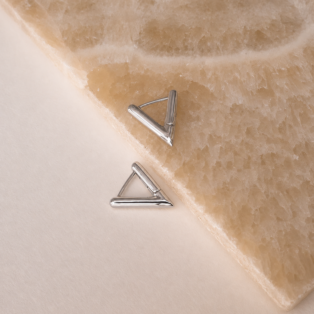 Pair of silver triangle earrings on a beige stone surface