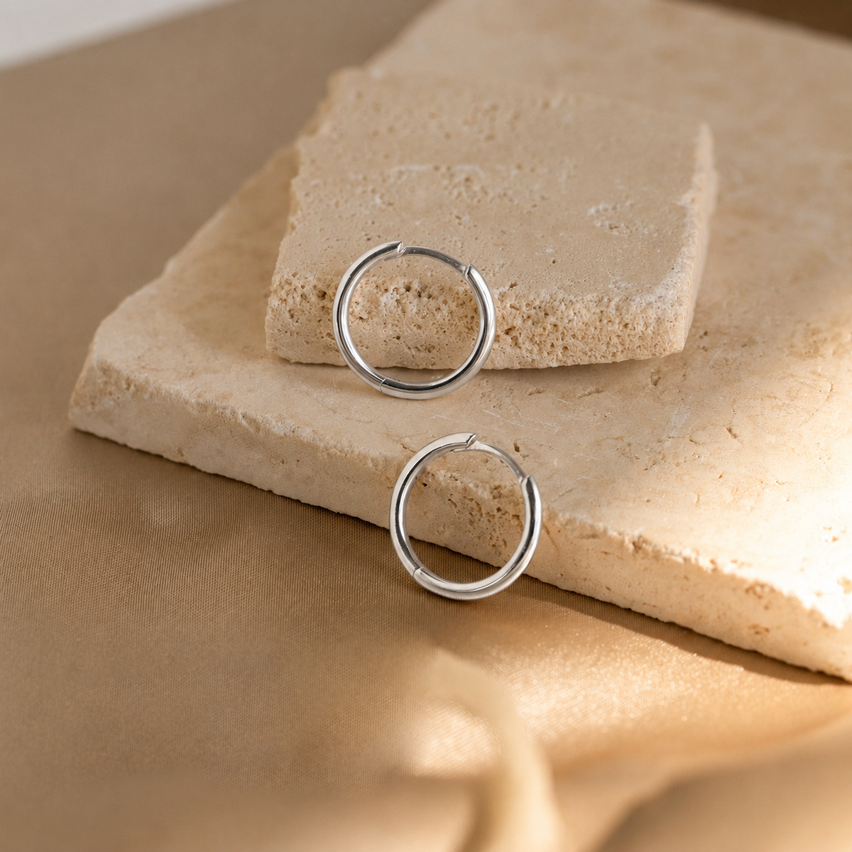 Silver hoop earrings on a beige stone surface