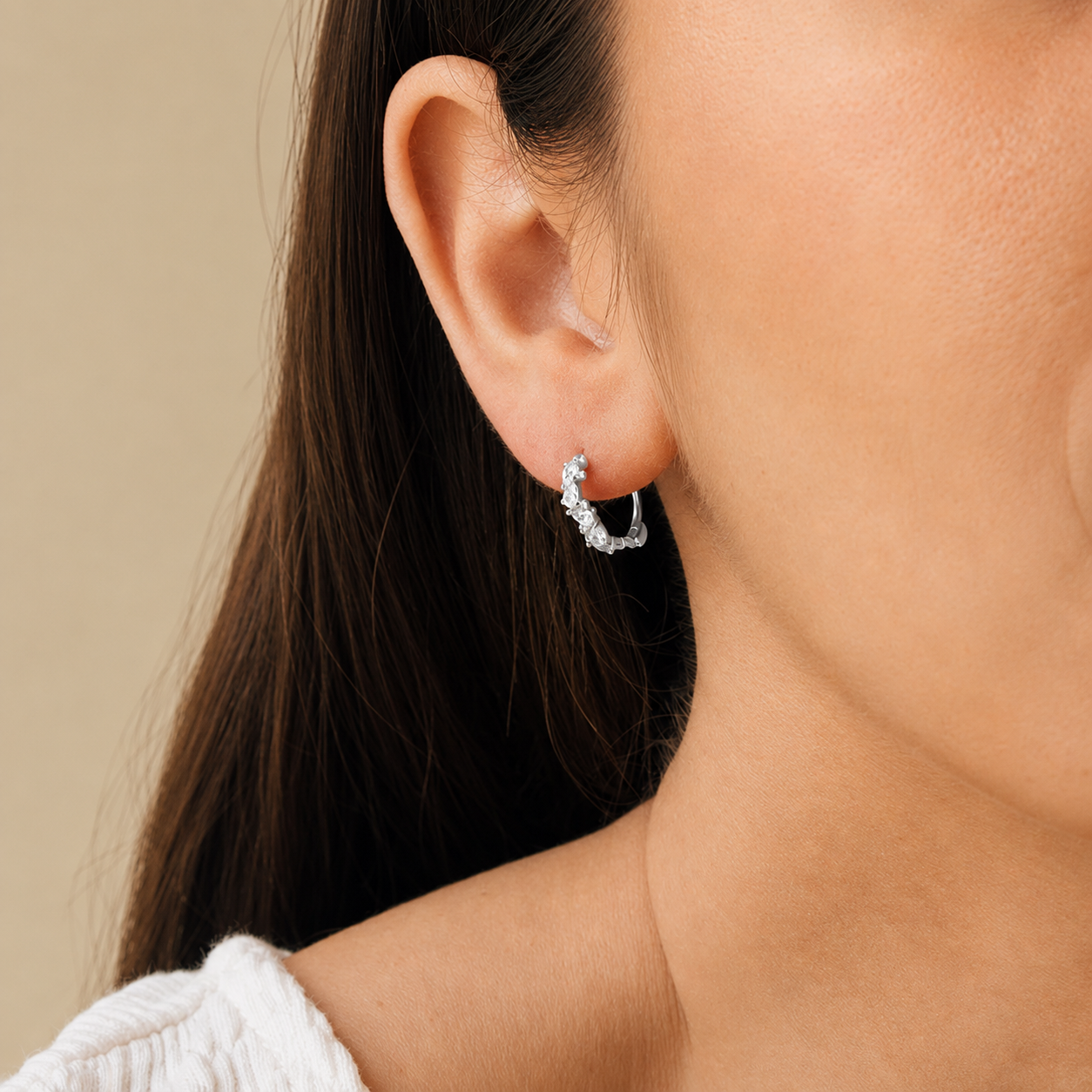 Close-up of a woman wearing a silver hoop earring against a neutral background