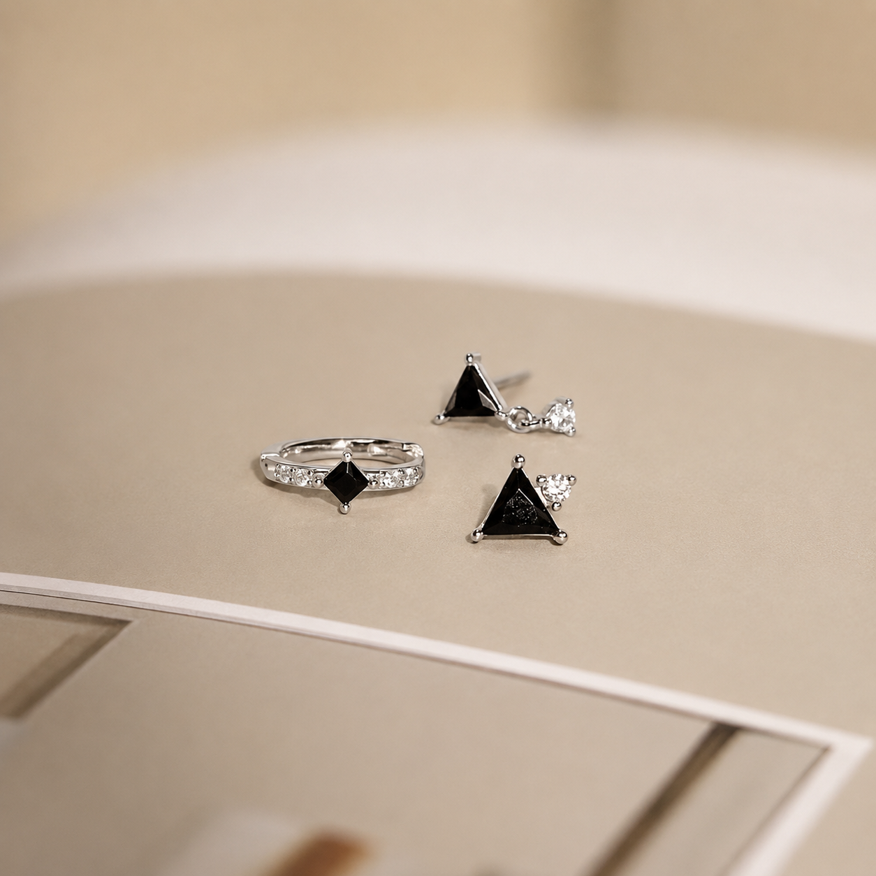 Silver ring and earrings with black gemstones on a beige surface