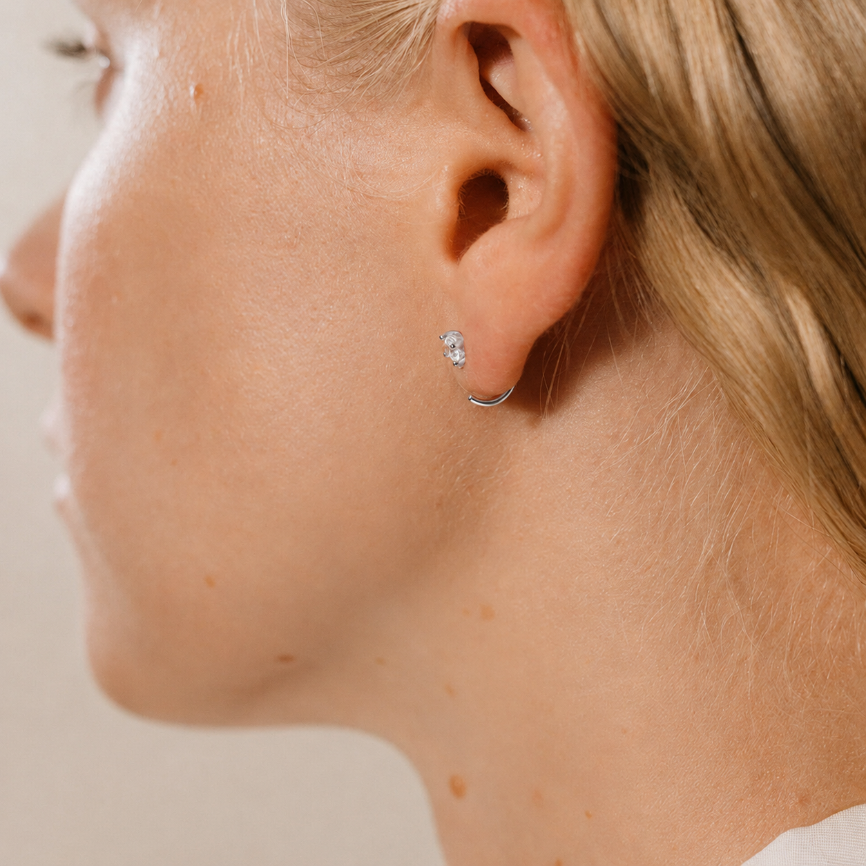 Close-up of a person wearing a silver hoop earring on a neutral background