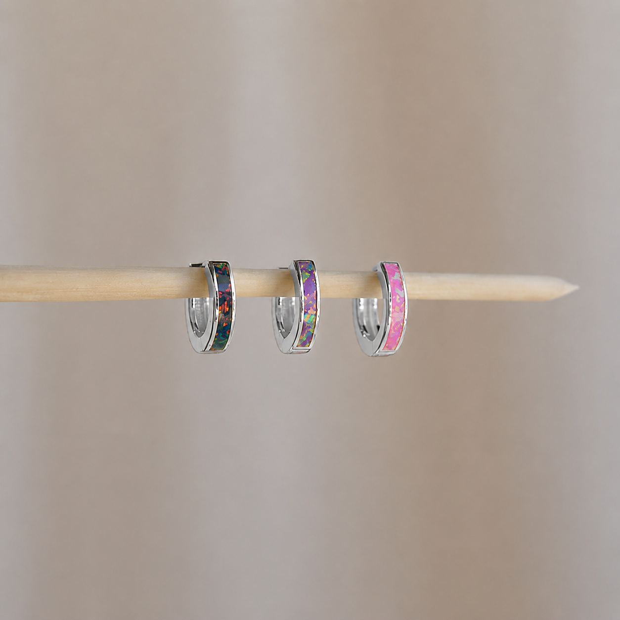 Three small hoop earrings with colorful centers on a wooden stick against a beige background
