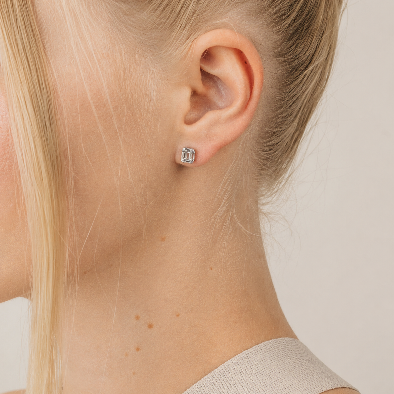 Close-up of a person wearing a silver stud earring on a neutral background