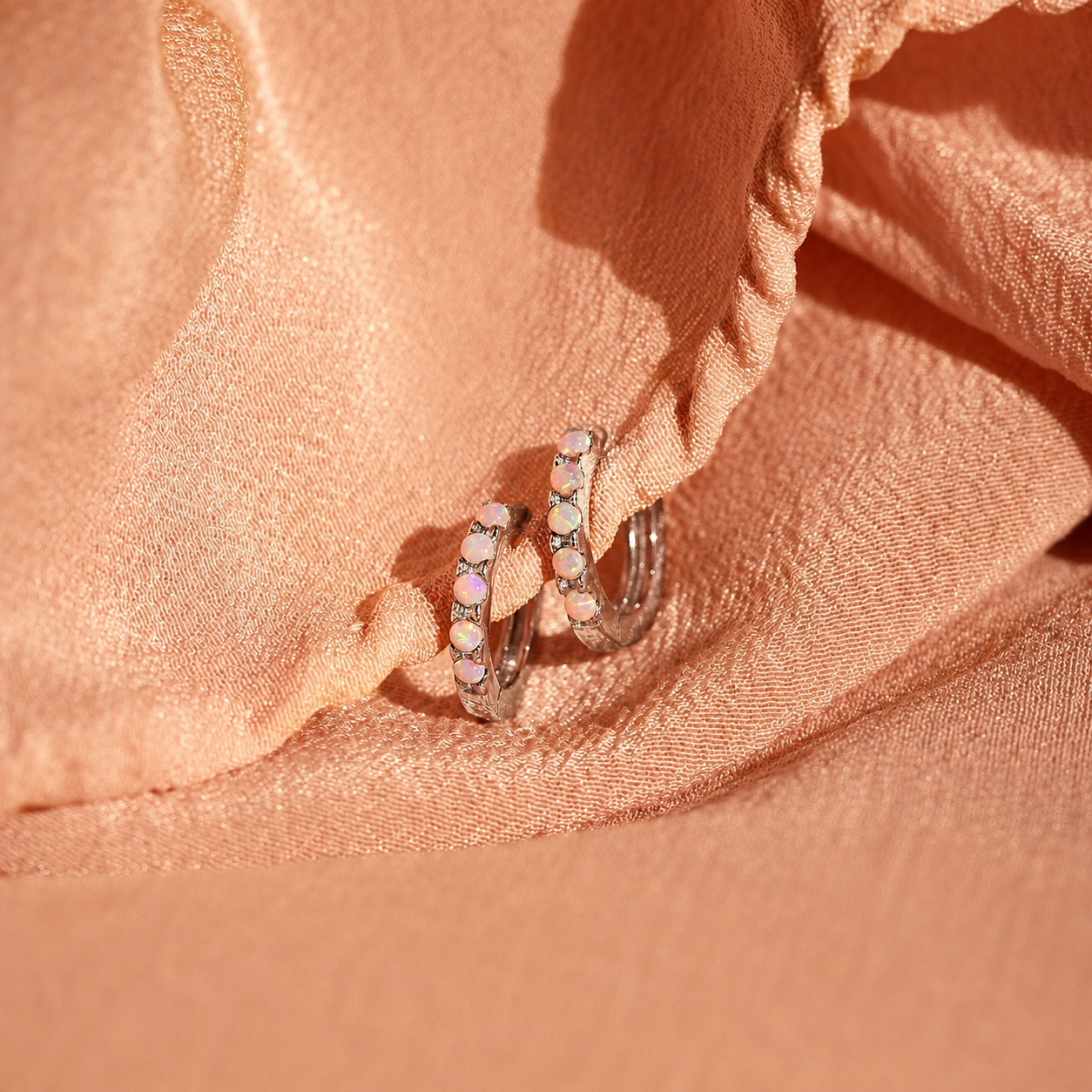 Pair of silver hoop earrings with small stones on a pink fabric background
