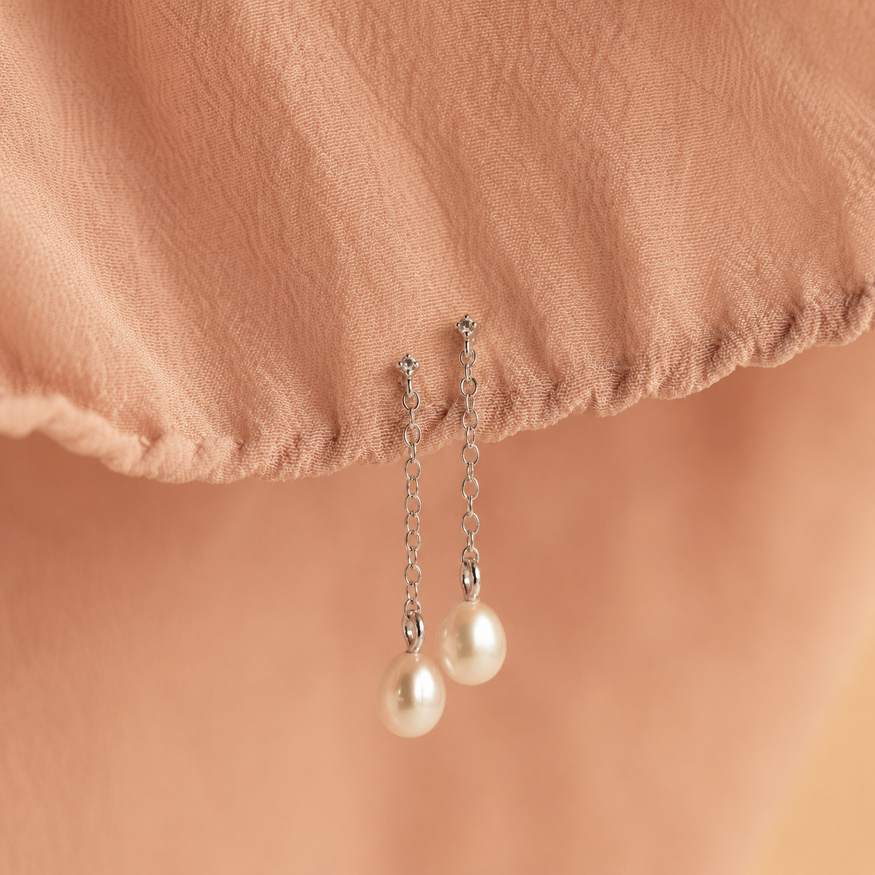 Pearl earrings on a soft pink fabric background