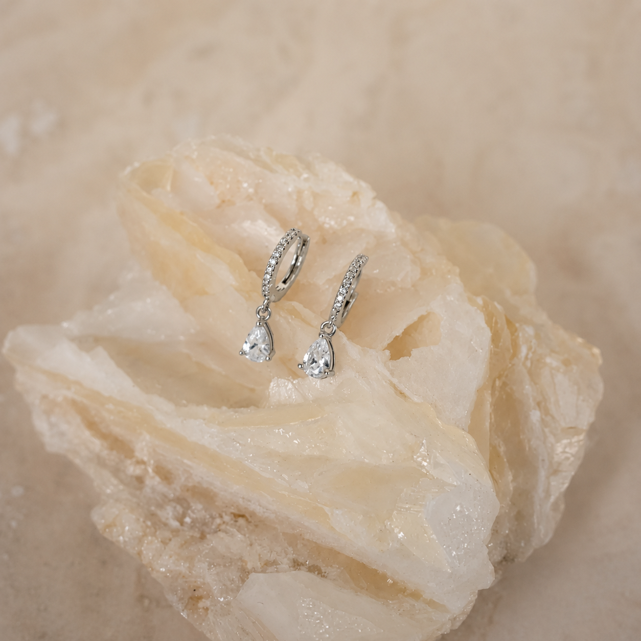 Silver teardrop earrings on a textured beige surface