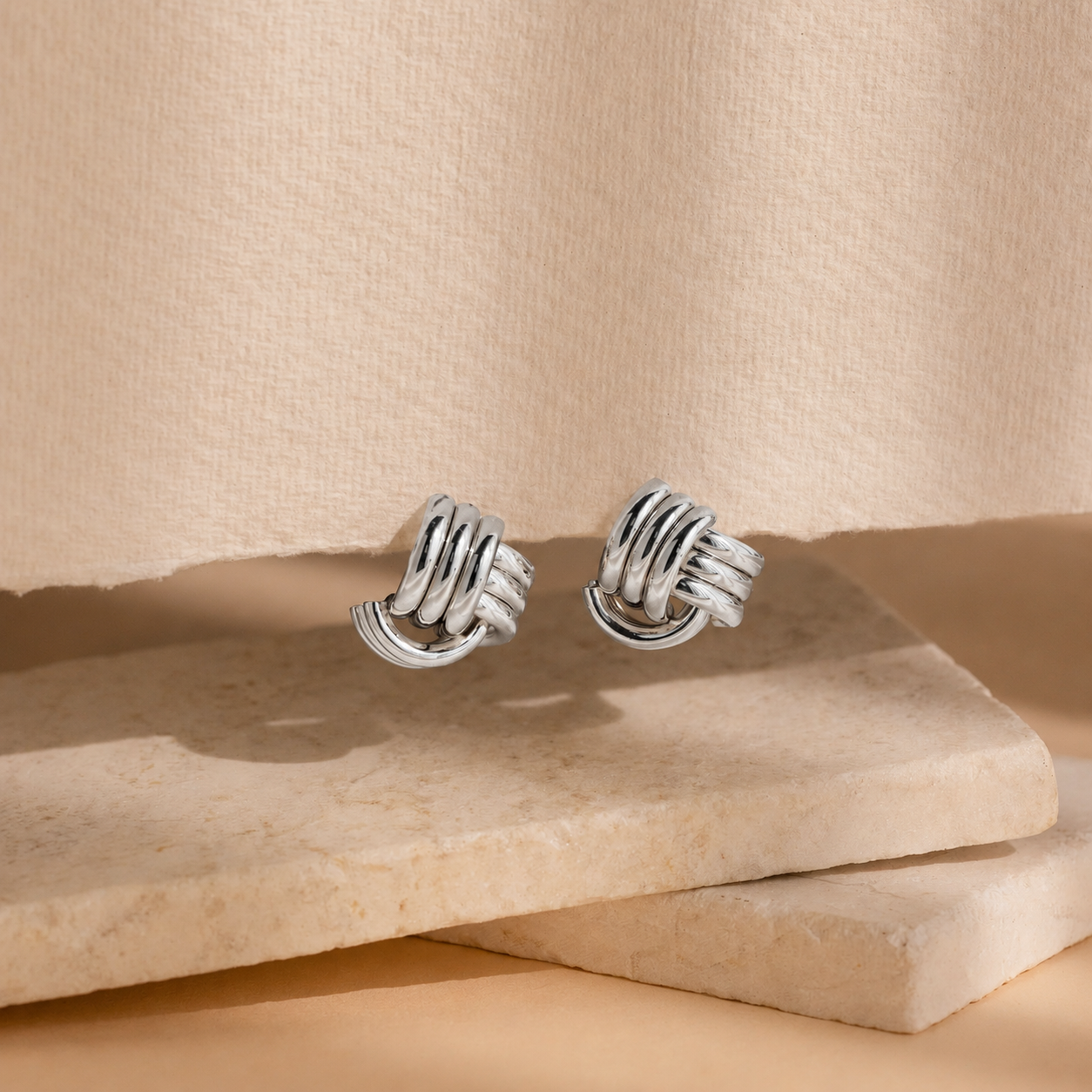 Pair of silver knot earrings on a beige stone surface