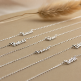 Silver name bracelets on a beige surface with dried grass in the background