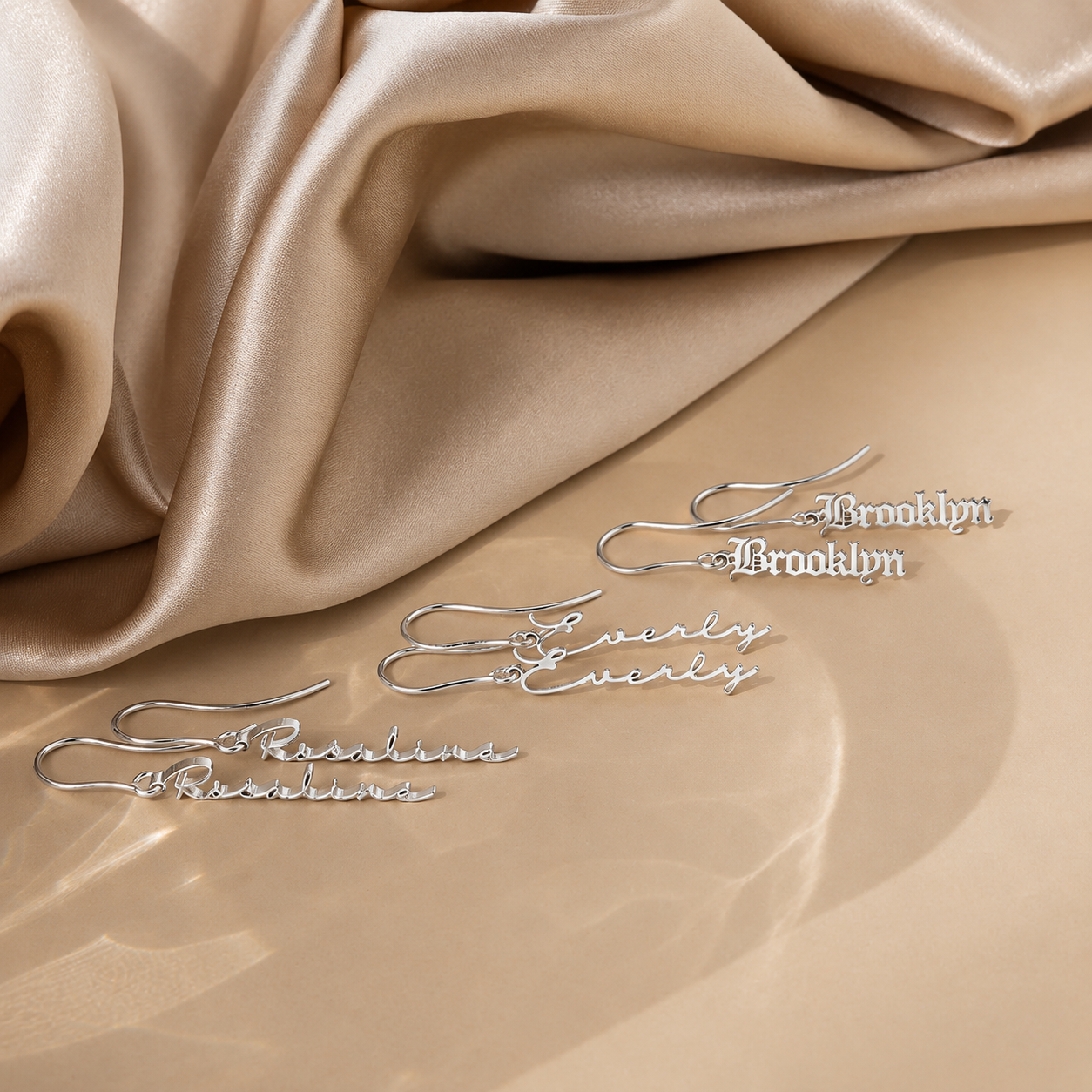 Silver earrings with 'Brooklyn' and 'Evelyn' text on beige fabric