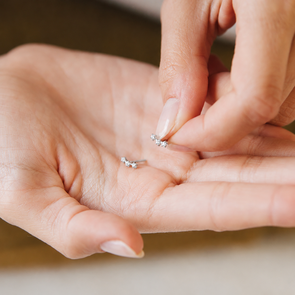 Close-up of hands holding small silver earrings.