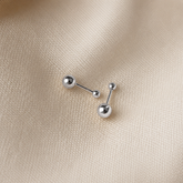 Two silver ball stud earrings on a textured beige fabric background.