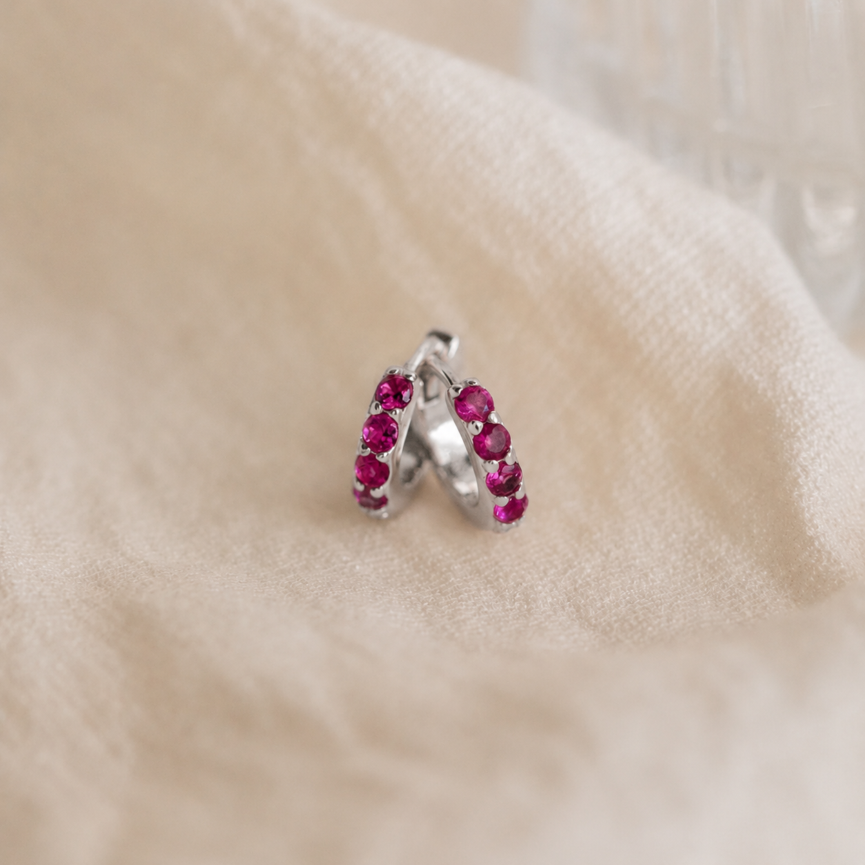 Silver earring with red gemstones on a beige fabric background