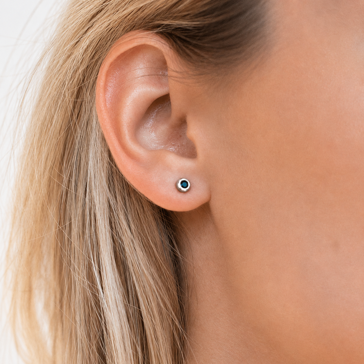 Close-up of an ear wearing a small stud earring with a green gemstone.