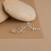 Silver name earrings on a brown surface with stones in the background