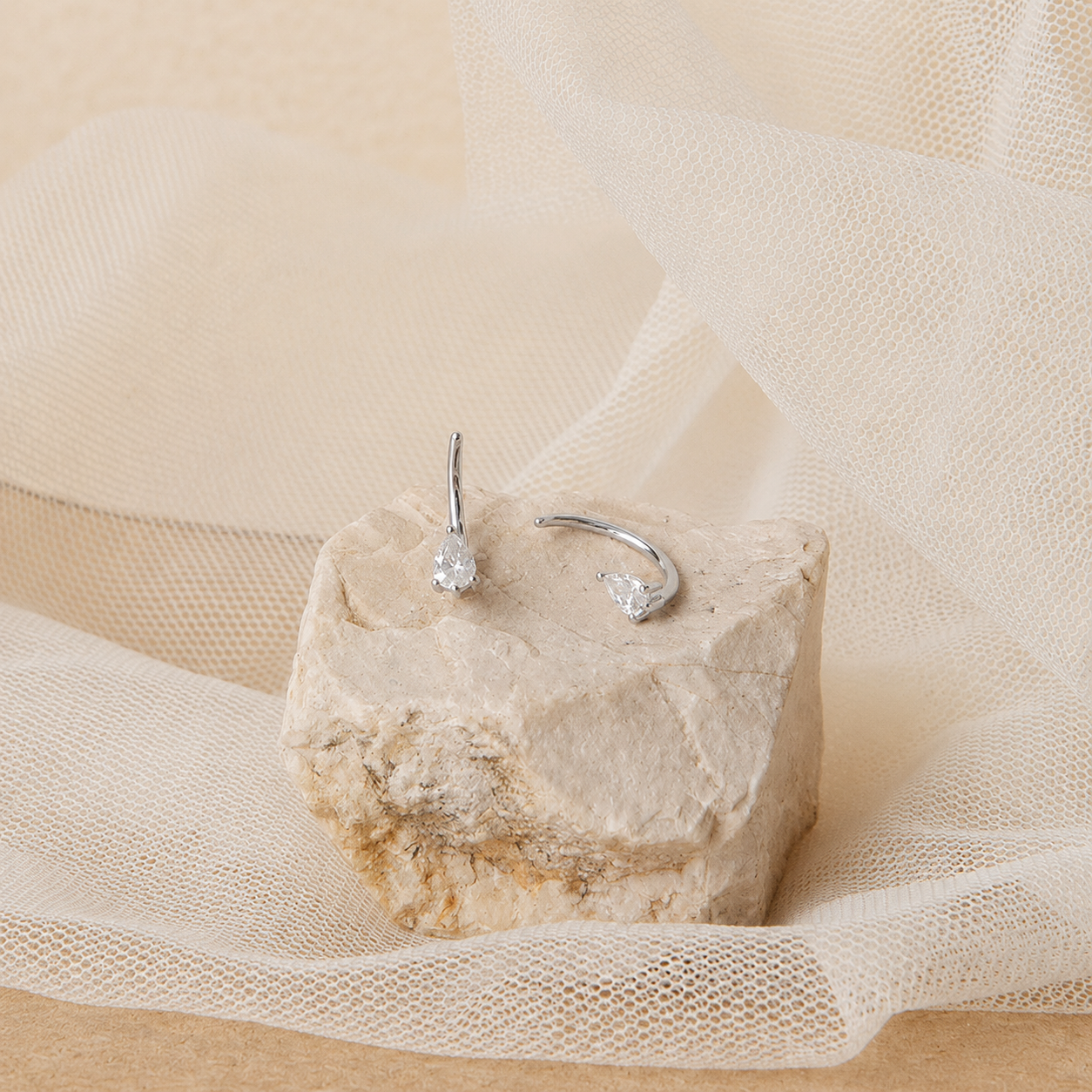 Silver hoop earrings on a textured stone surface with a soft beige background