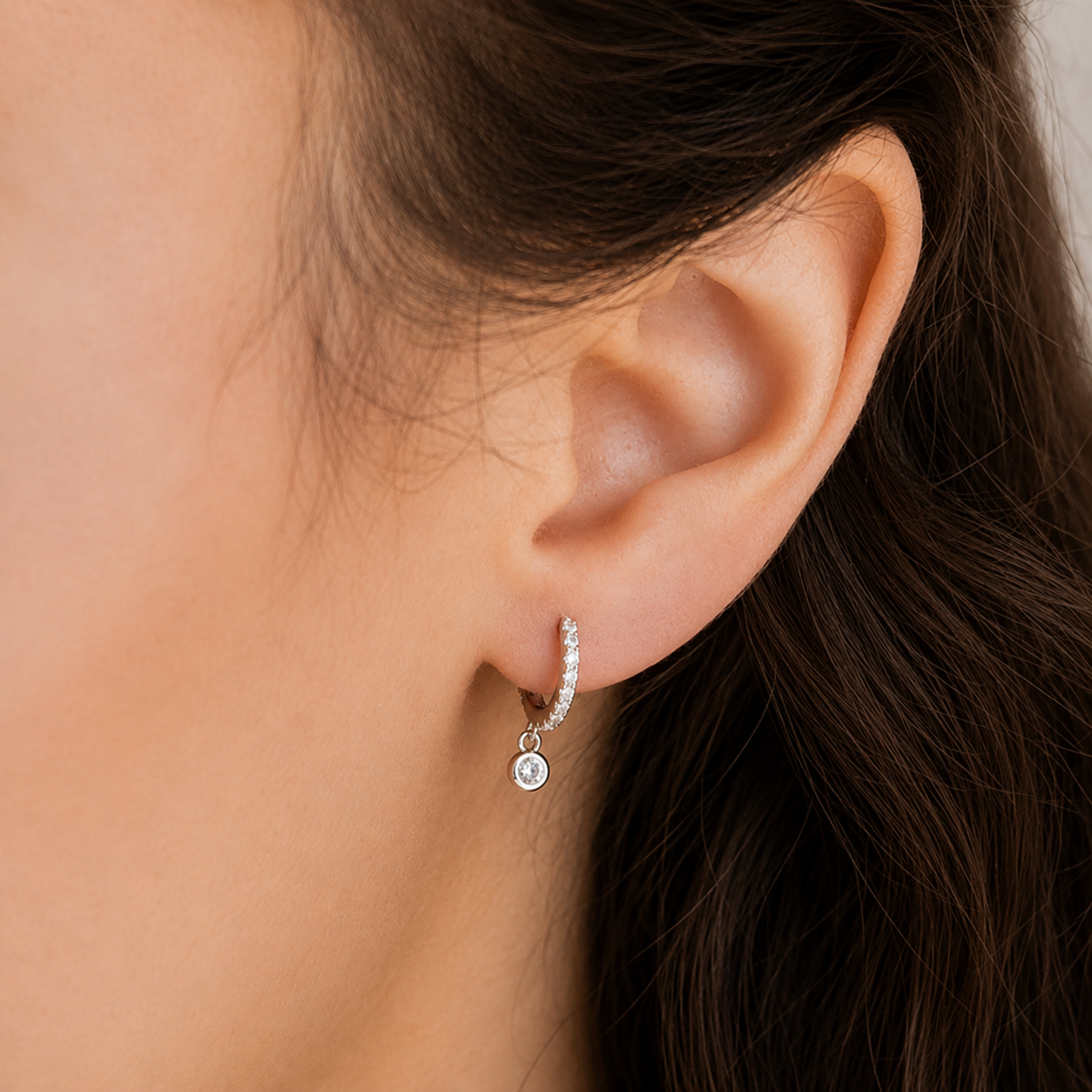Close-up of an ear wearing a silver hoop earring with a small round pendant.