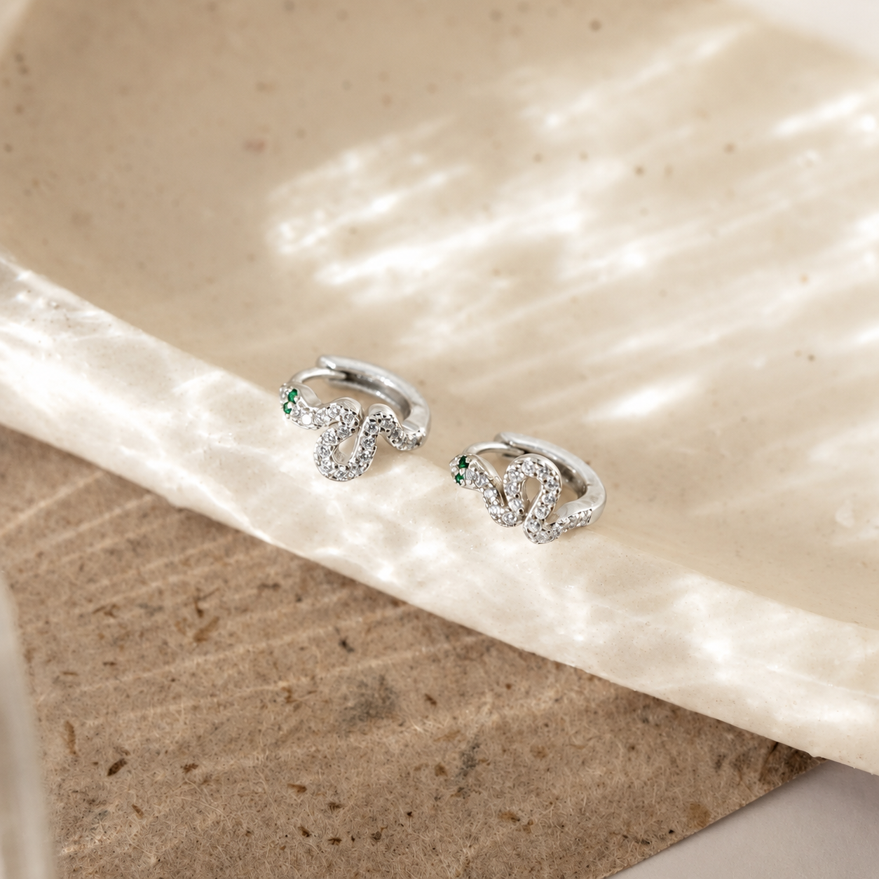 Silver hoop earrings with gemstones on a textured beige surface