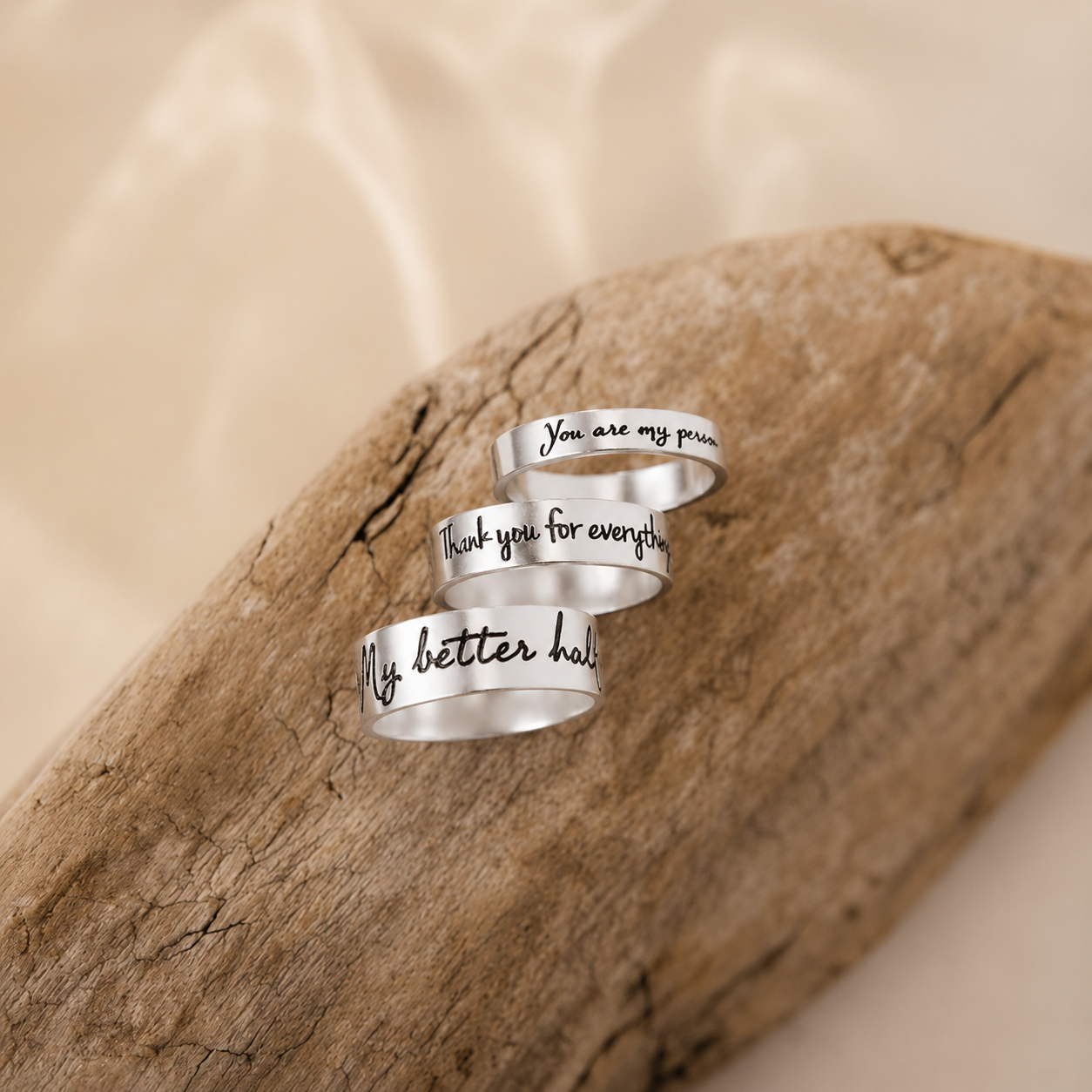Three silver wrap-around rings with engraved text on a wooden surface