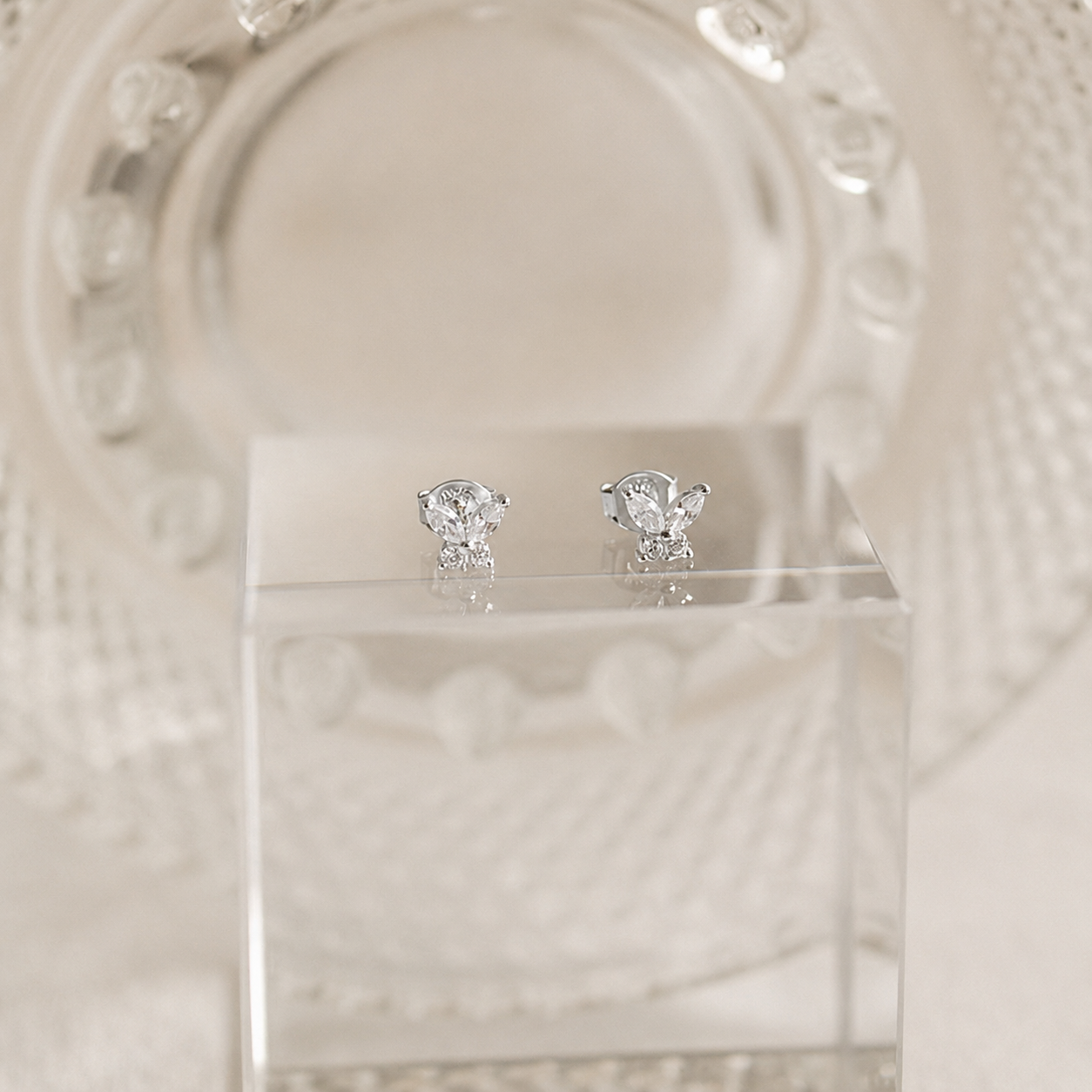 Pair of diamond stud earrings on a clear stand with a decorative white background