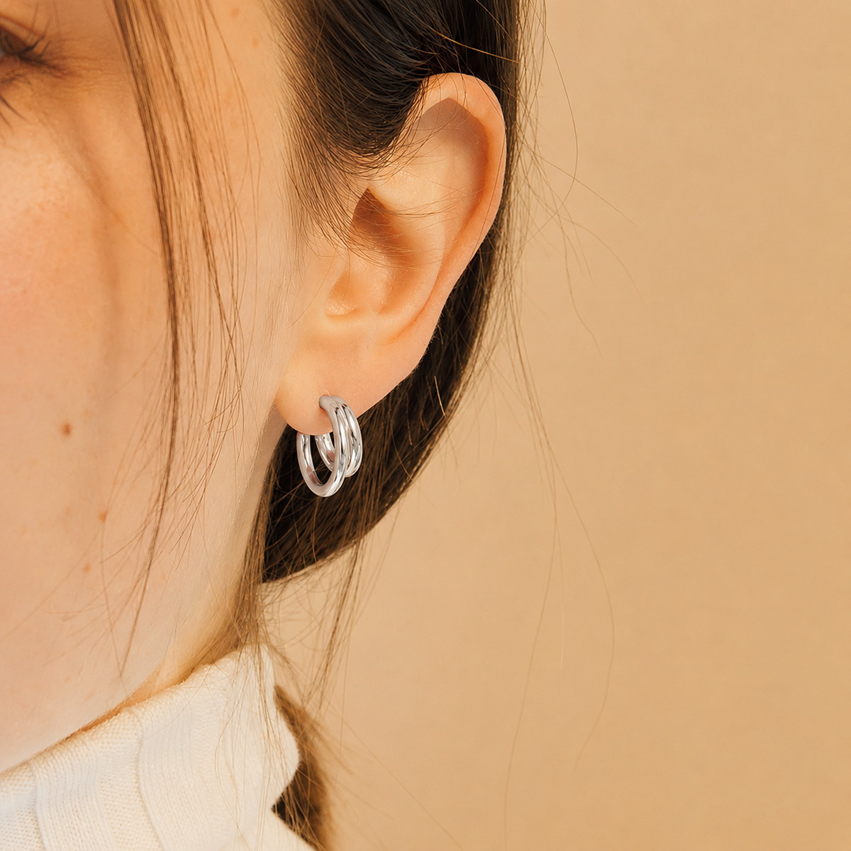 Close-up of an ear wearing a silver hoop earring on a beige background