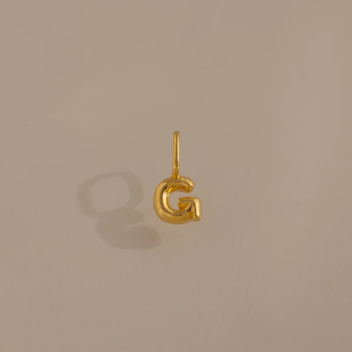 Gold letter 'G' pendant on a beige background