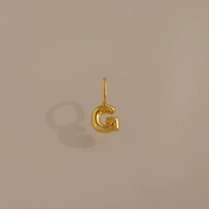 Gold letter 'G' pendant on a beige background
