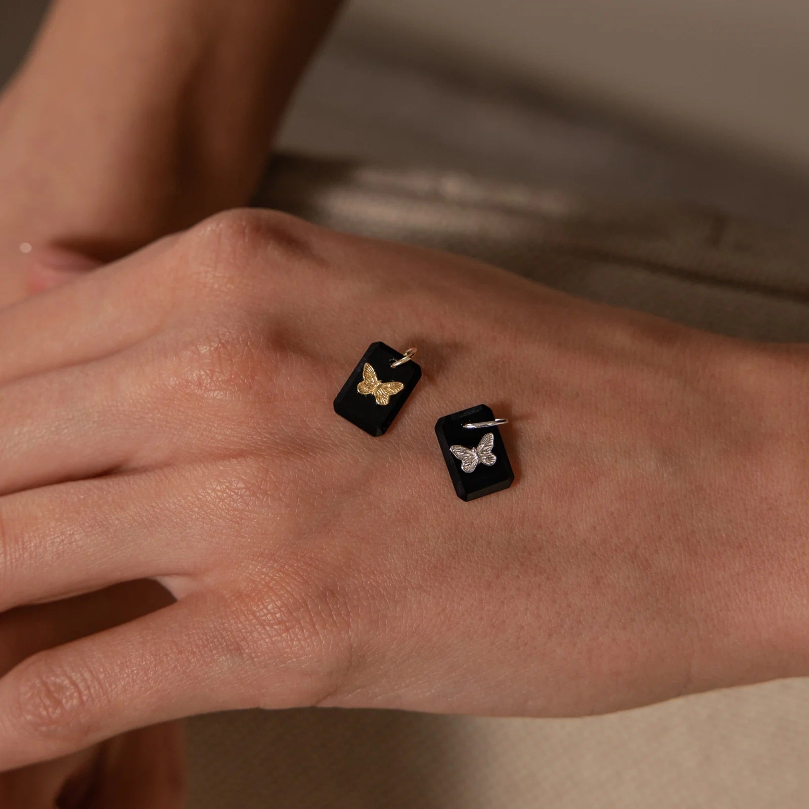 Butterfly earrings on a person's wrist with a neutral background