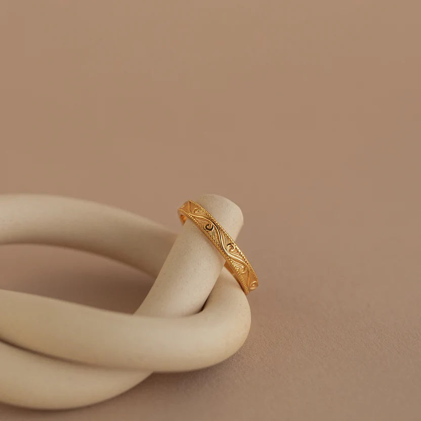 Gold ring with intricate design on a beige ceramic object against a beige background