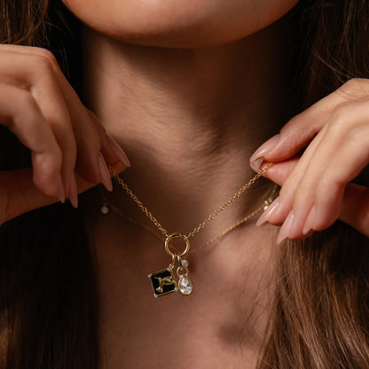 Close-up of a gold necklace with charms being adjusted by hands.