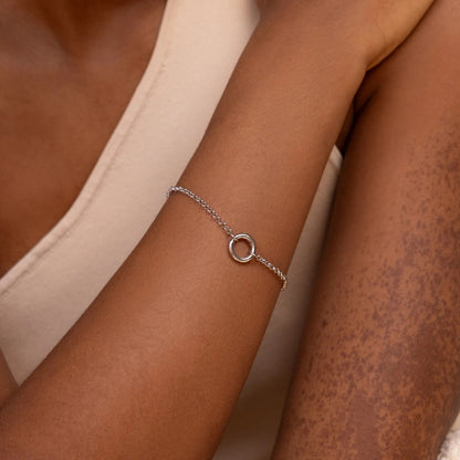 Silver bracelet with a circular charm on a person's wrist against a neutral background