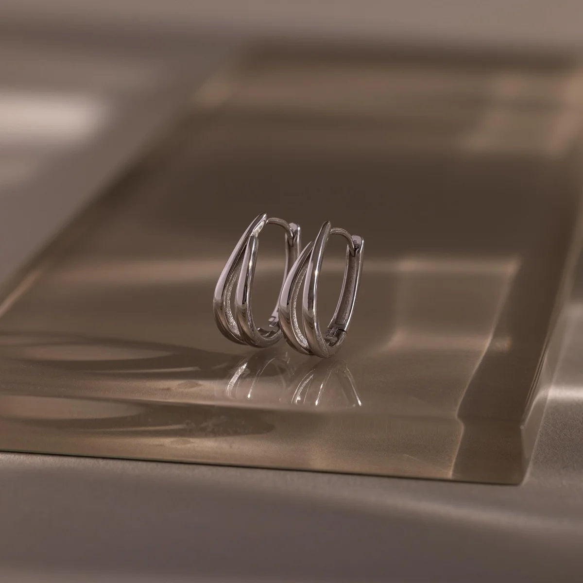 Pair of silver hoop earrings on a reflective metallic surface