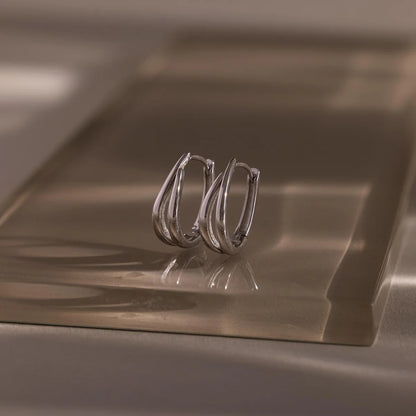 Pair of silver hoop earrings on a reflective metallic surface