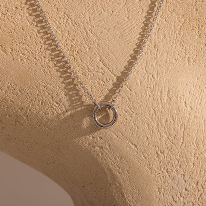 Silver necklace with a ring pendant on a beige textured surface
