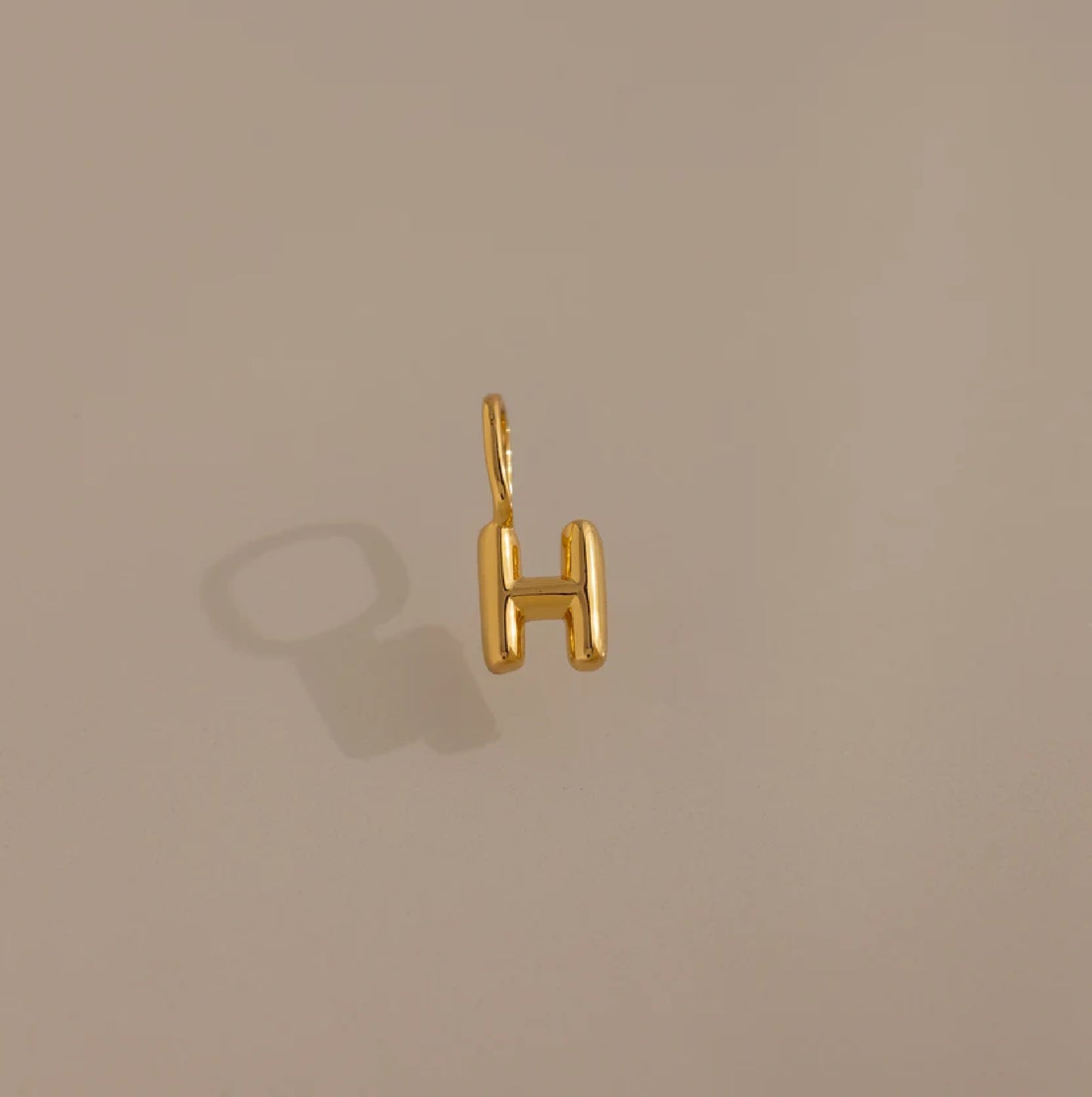 Gold 'H' shaped pendant on a beige background