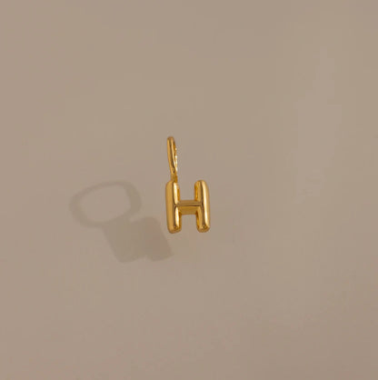 Gold 'H' shaped pendant on a beige background
