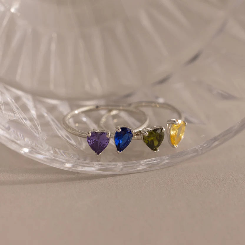 Silver ring with heart-shaped gemstones on a clear glass stand.