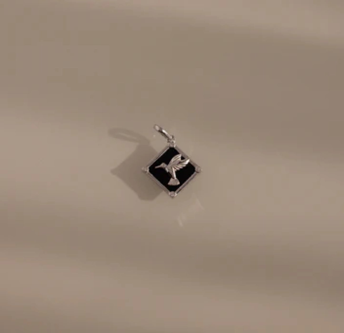 Silver pendant with a black square design on a beige background
