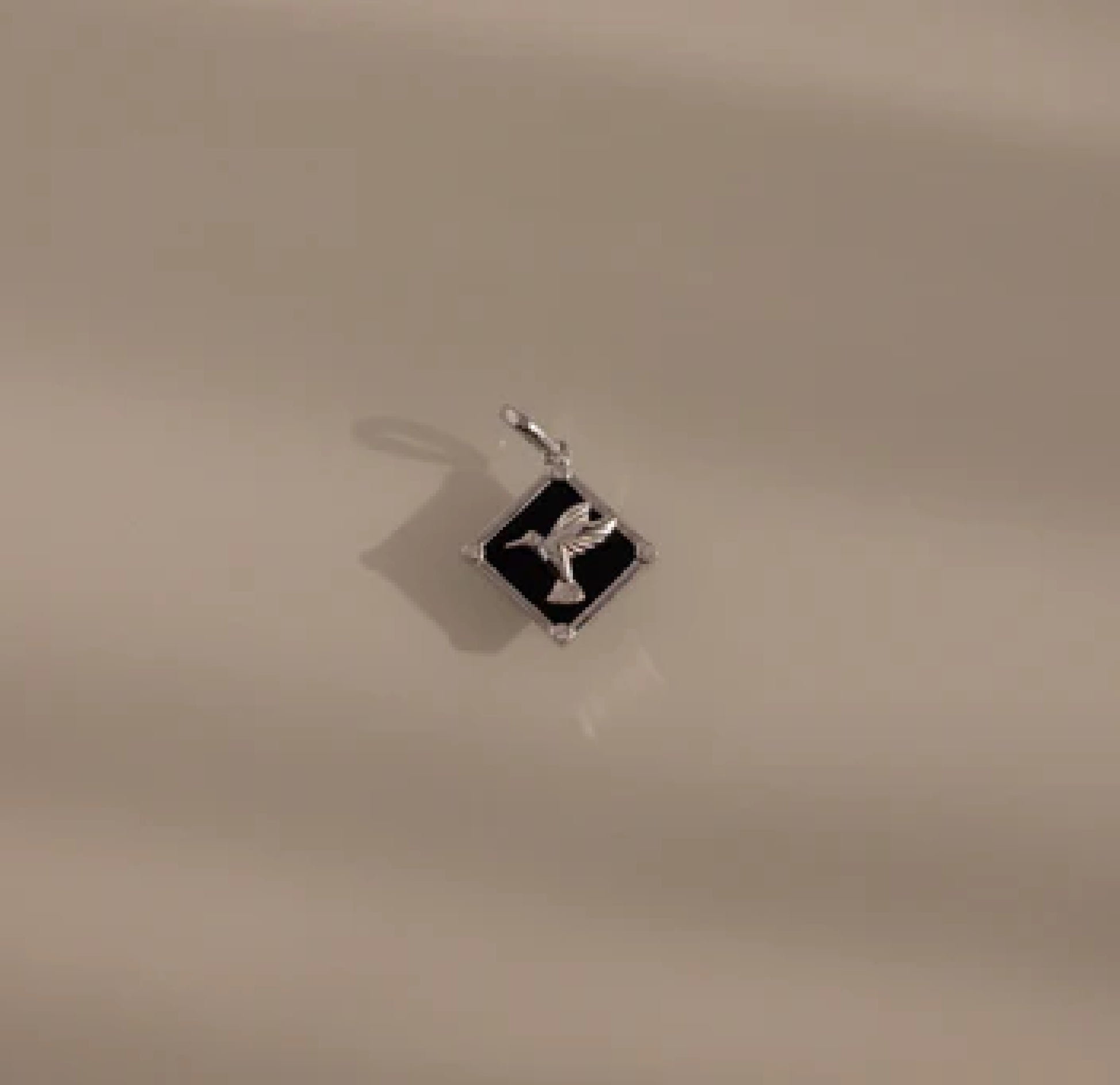 Silver pendant with a black square design on a beige background