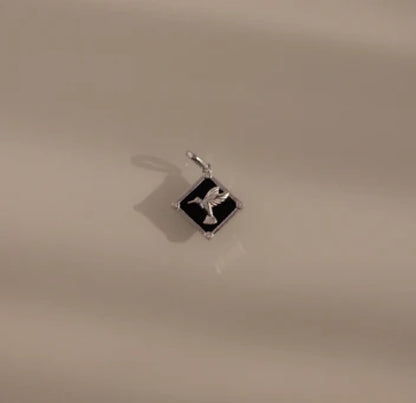 Silver pendant with a black square design on a beige background